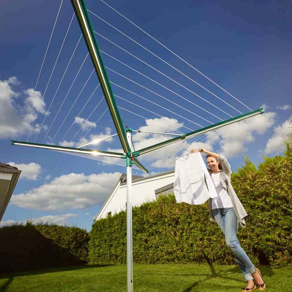 Eine Person hängt Kleidung an einen Wäscheständer im Garten auf. Im Hintergrund sind blauer Himmel und Wolken zu sehen.