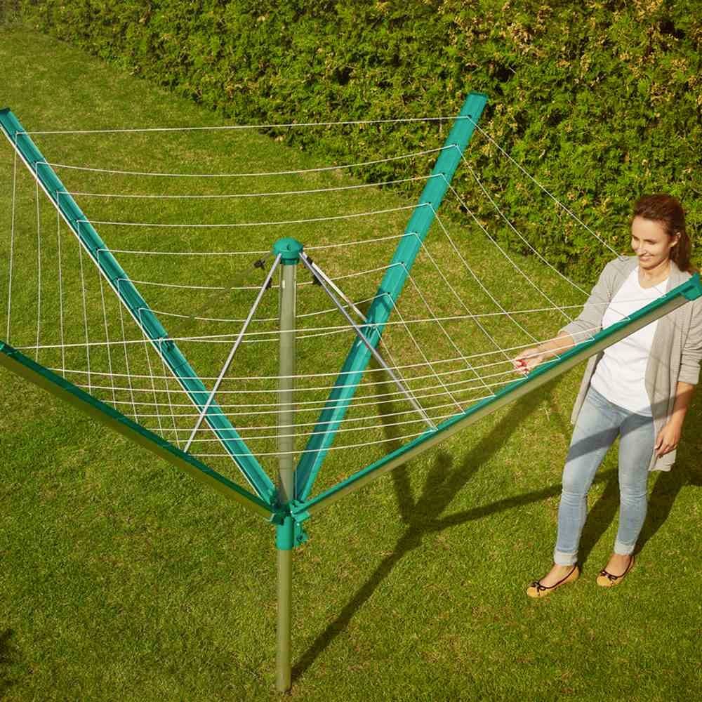 Eine Frau steht neben einem Wäscheschirm in einem Garten. Der Wäscheschirm ist geöffnet und bereit zum Aufhängen von Kleidung.