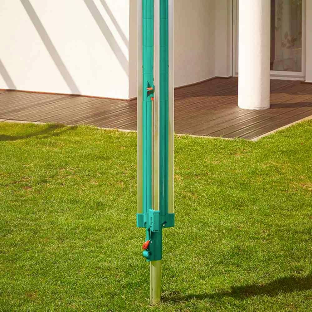 Ein grüner Sonnenschirmständer auf einem Rasen vor einem Haus mit Holzterrasse und weißen Wänden.