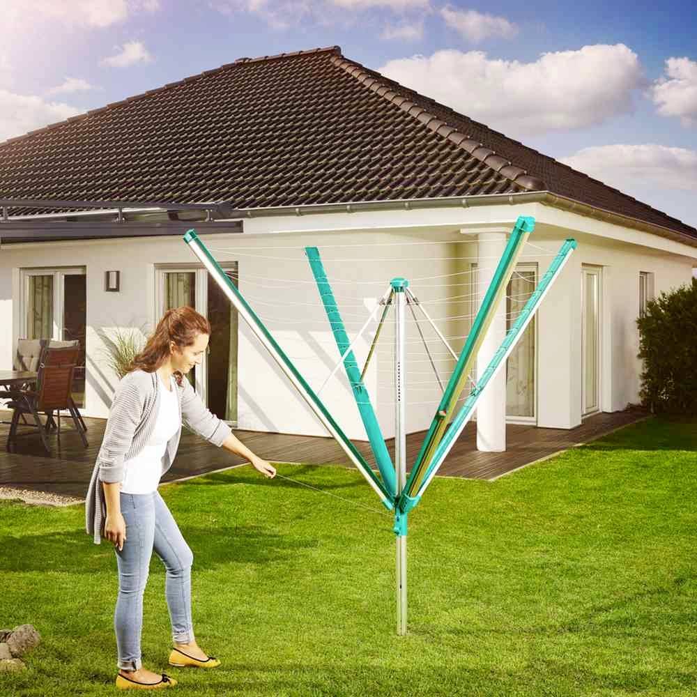 Eine Frau stellt einen Wäscheständer in einem sonnigen Garten auf. Im Hintergrund befindet sich ein modernes Haus mit Terrasse.