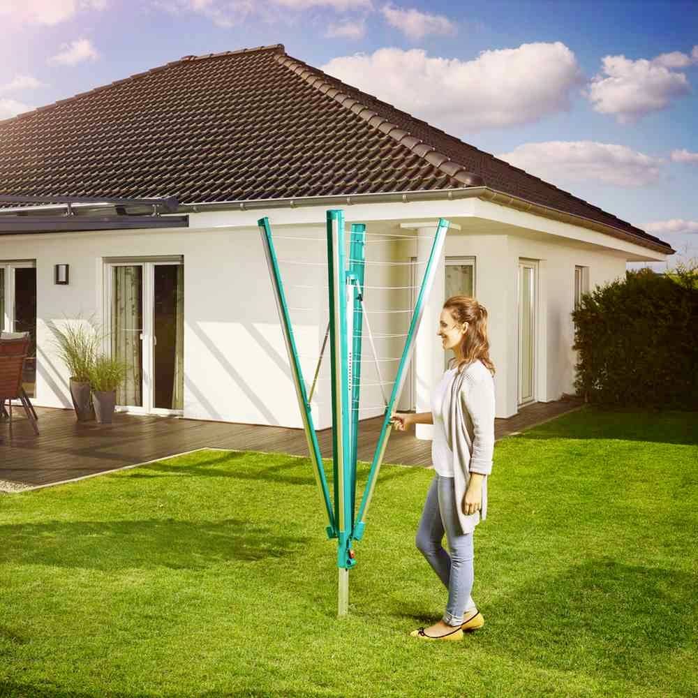 Eine Frau steht im Garten neben einem zusammengeklappten Wäschetrockner. Im Hintergrund ist ein modernes Einfamilienhaus zu sehen.