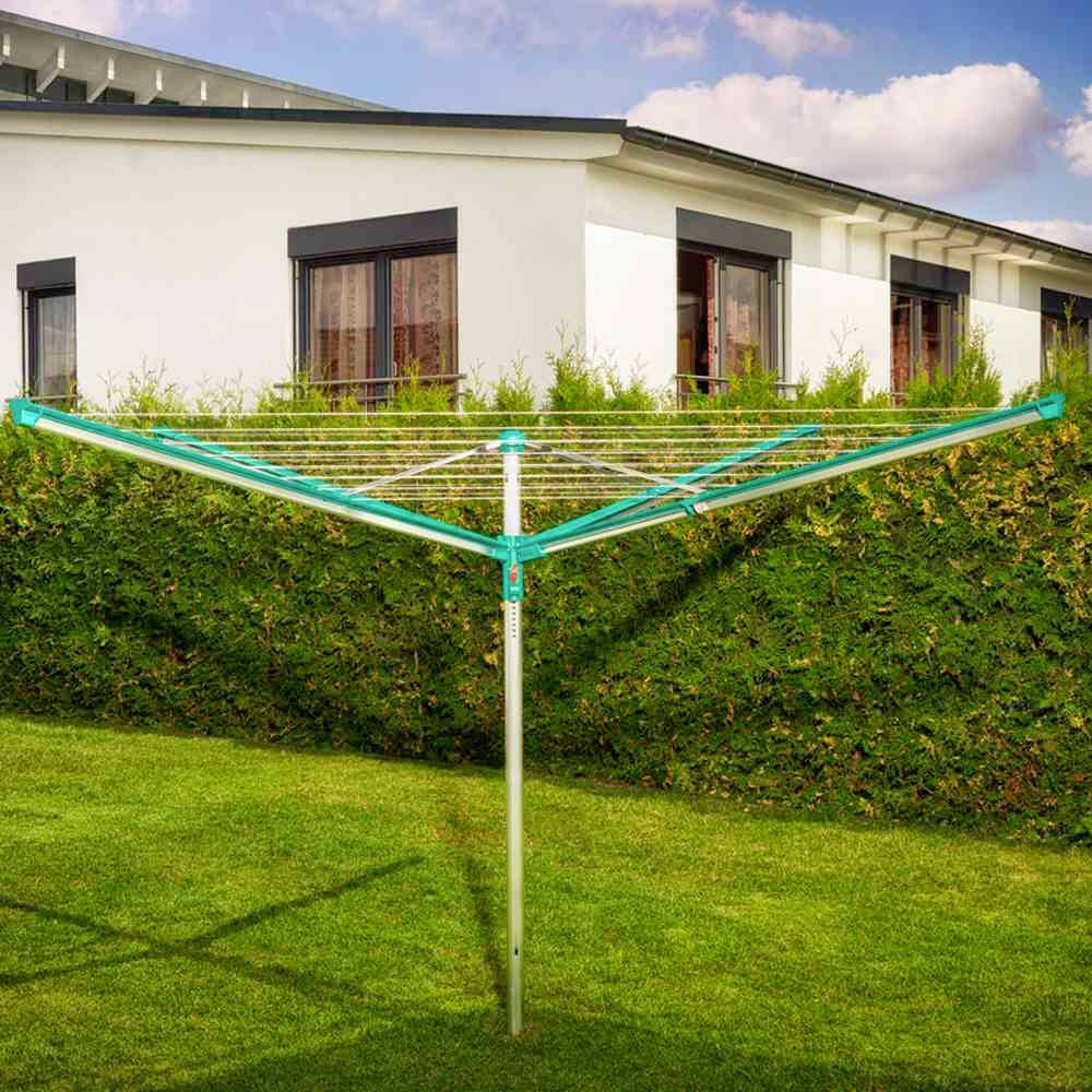 Ein ausklappbarer Wäschetrockner steht im Garten vor einer grünen Hecke, im Hintergrund ein weißes Haus mit mehreren Fenstern.