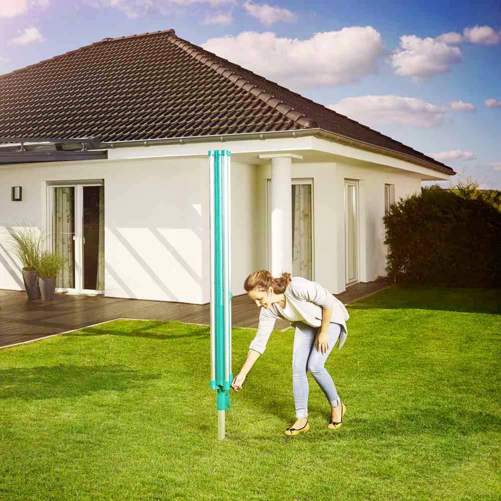 Eine Frau installiert einen Wäscheständer im Garten. Im Hintergrund ist ein weißes Haus mit Terrasse und Pflanzen zu sehen.