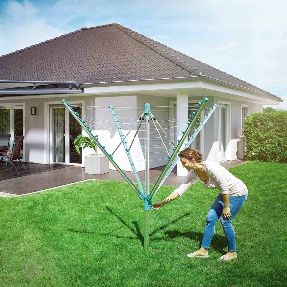 Eine Frau hängt Wäsche an einem Wäschespinne im Garten vor einem modernen Einfamilienhaus auf.