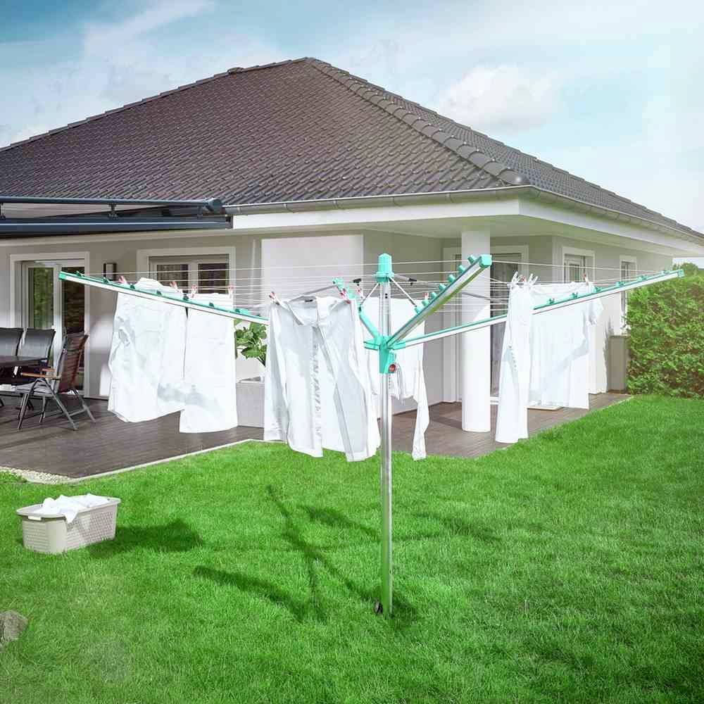 Weiße Kleidung hängt an einem Wäscheschirm im Garten vor einem modernen Haus. Frische, sonnige Atmosphäre.