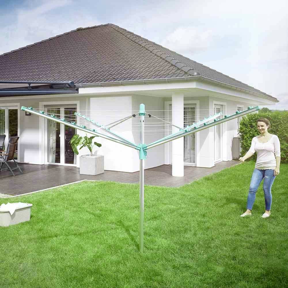 Eine Frau steht im Garten neben einem Wäschespinner mit einer Rasenfläche und einem Haus im Hintergrund.