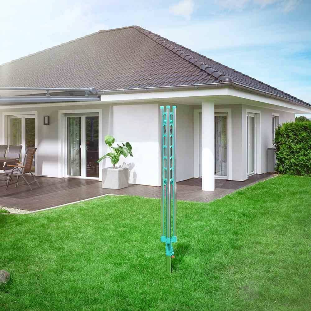 Ein modernes Haus mit Terrasse, Gartenmöbeln und grünem Rasen. Im Vordergrund steht ein Wäschespindelgestell im Garten.