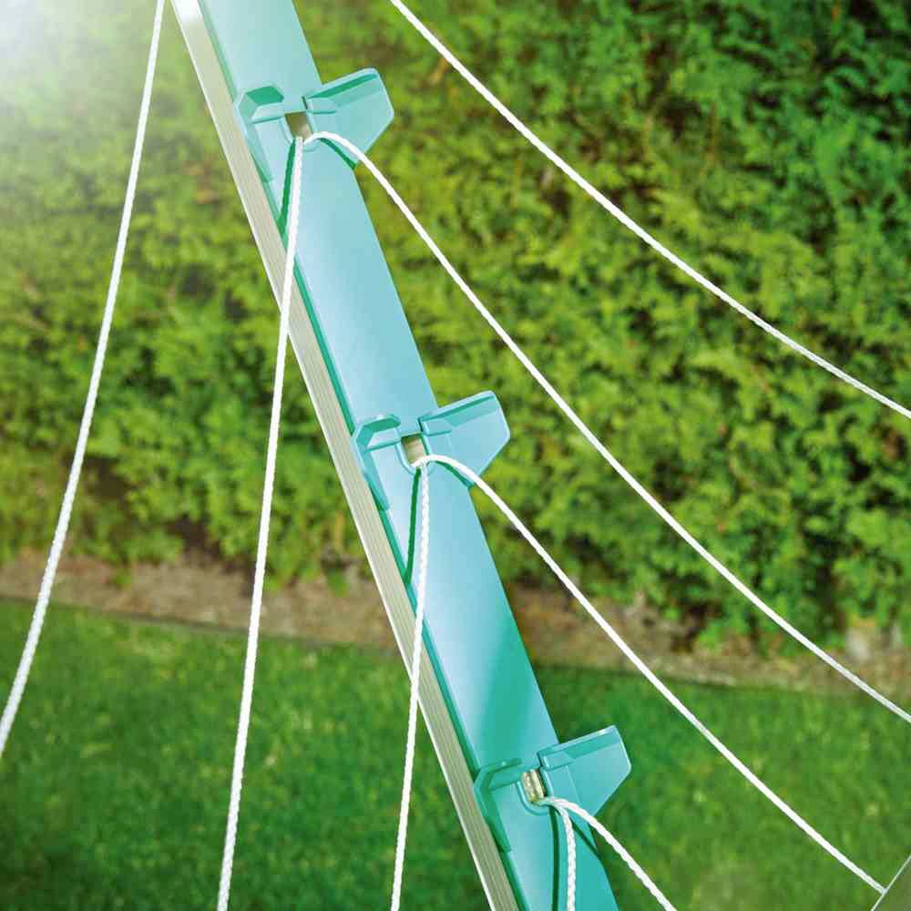 Ein türkisfarbener Wäscheständer steht in einem Garten. Mehrere Schnüre sind straff gespannt, um Wäsche zu trocknen. Im Hintergrund sind grüne Büsche sichtbar.