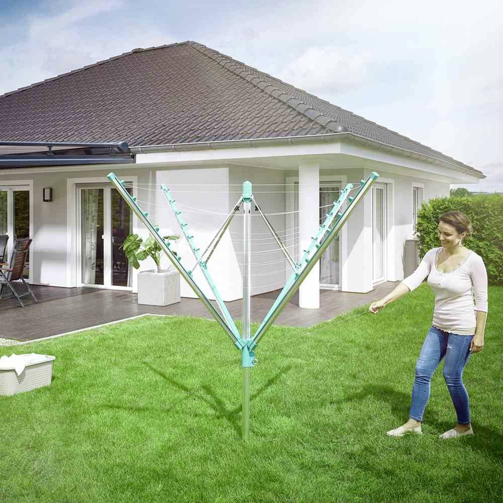 Frau im Garten geht auf einen Wäschespinnenständer zu, im Hintergrund ein modernes Haus mit Terrasse.