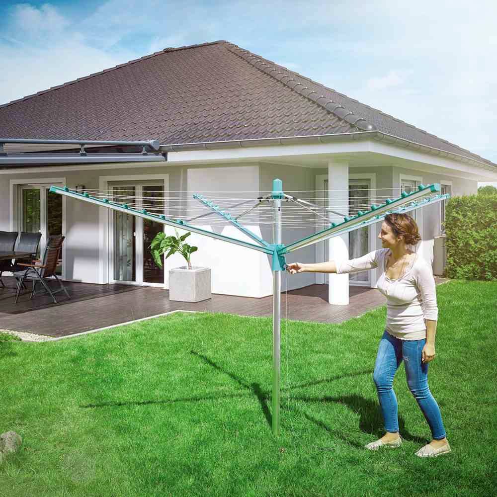 Eine Frau steht im Garten vor einem modernen Haus und dreht einen Wäscheschirm. Der Himmel ist klar und das Gras ist grün.