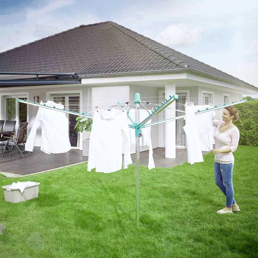 Eine Frau hängt weiße Kleidung an einem Wäschetrockner in einem Garten auf, neben einem modernen Bungalow.