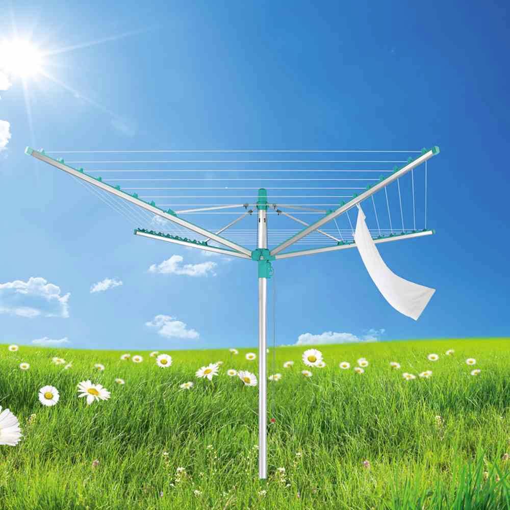 Wäschespinne auf einer Wiese mit Gänseblümchen unter blauem Himmel und Sonne, ein Handtuch hängt daran.