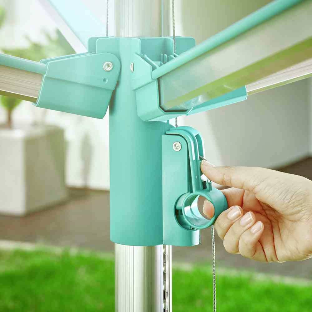 Jemand öffnet einen türkisfarbenen Wäscheschirmmechanismus im Garten. Eine Hand betätigt den Hebel am Ständer.