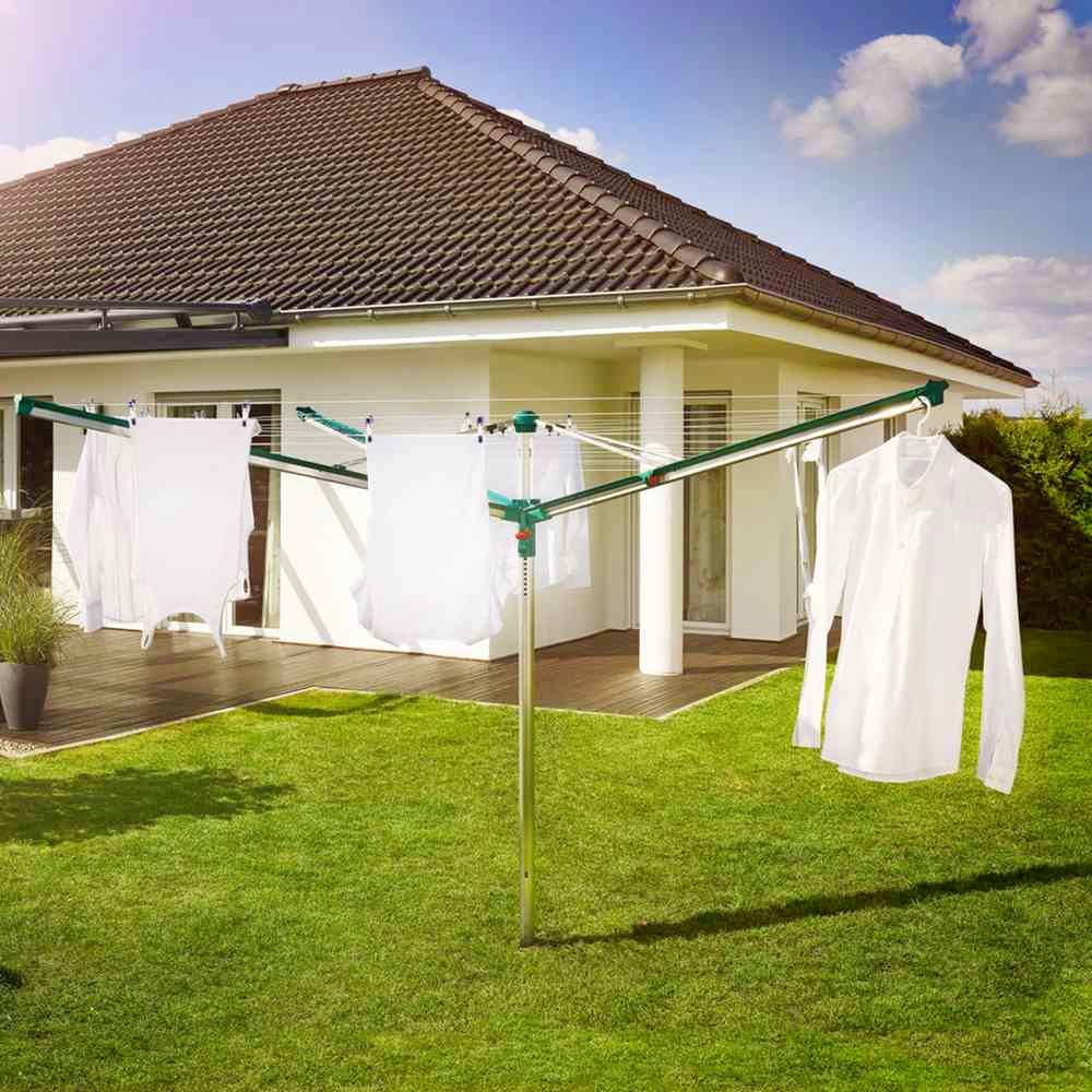 Ein weißes Hemd und andere Kleidung hängen an einem Wäscheständer im Garten vor einem weißen Haus mit roten Dachziegeln.