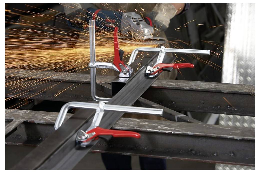 Ein Arbeiter, der ein eingespanntes Metallstück mit einem Winkelschleifer bearbeitet und dabei Funken über eine Werkstattarbeitsfläche verteilt.
