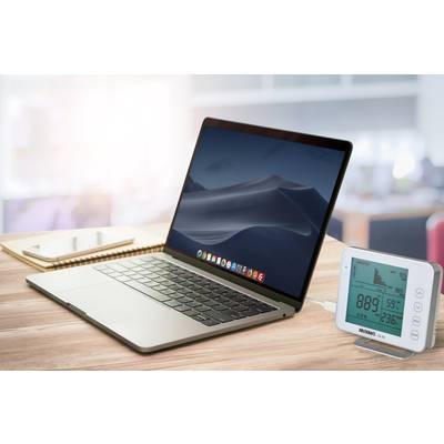 Ein Laptop auf einem Schreibtisch neben einem digitalen Thermo-Hygrometer und einem Notizbuch. Der Laptop zeigt einen neutralen Bildschirmhintergrund.