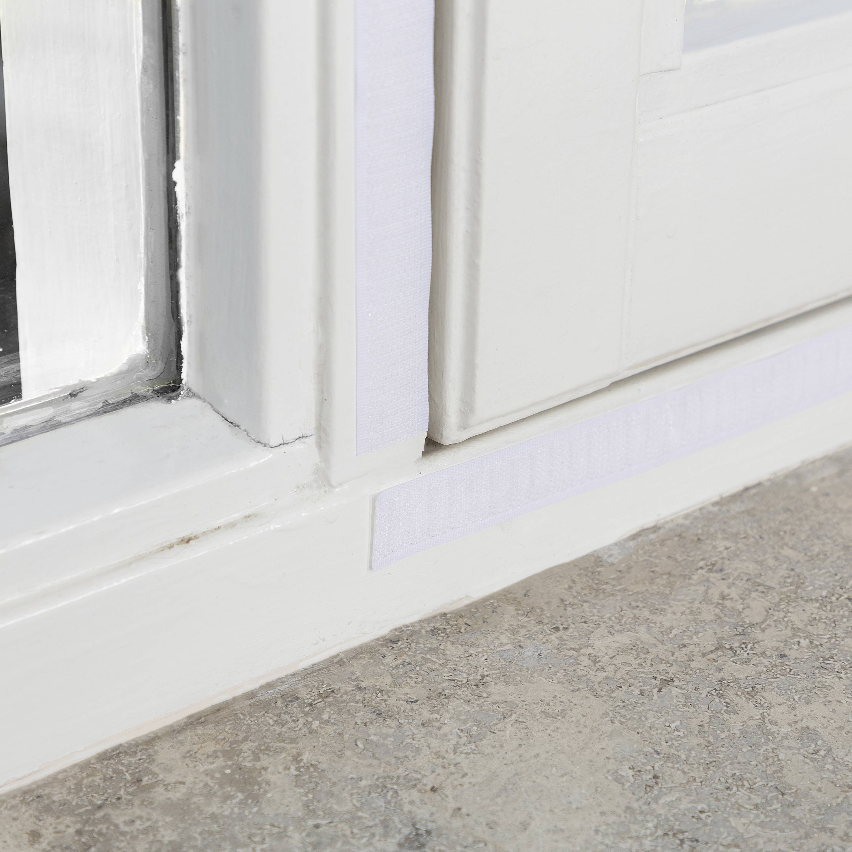 Weiße Fensterrahmen mit Klebestreifen an den Fugen, auf einem Steinboden.