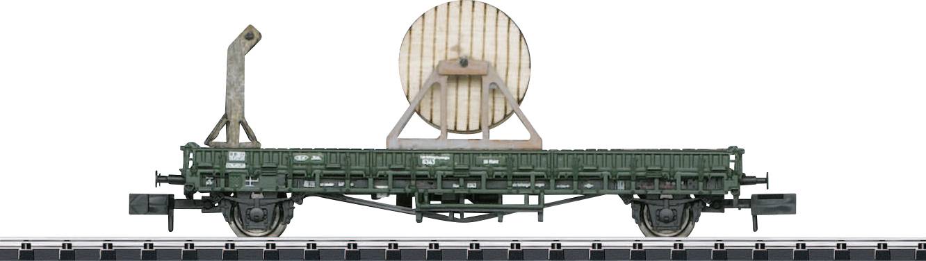 Ein grüner Güterwaggon mit einer großen Holzspule darauf. Der Waggon befindet sich auf Bahngleisen und hat eine aufrechte Metallstütze.