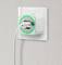 Ein weißer Stecker mit grünem LED-Ring ist in einer Steckdose an einer strukturierten Wand eingesteckt, symbolisiert aktiven Stromfluss.