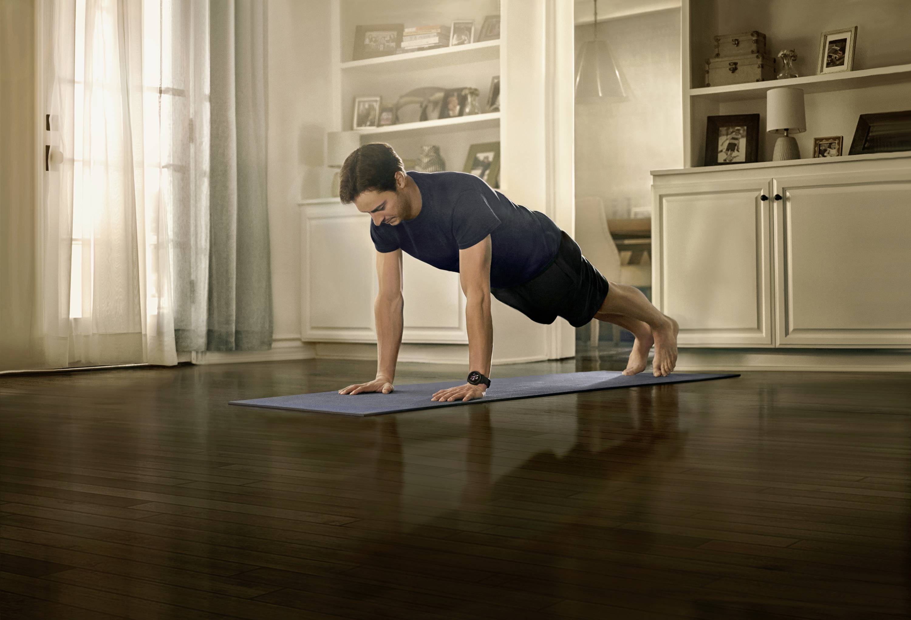 Ein Mann macht einen Liegestütz auf einer Yogamatte in einem gemütlichen Wohnzimmer mit Holzboden und Regalen im Hintergrund.