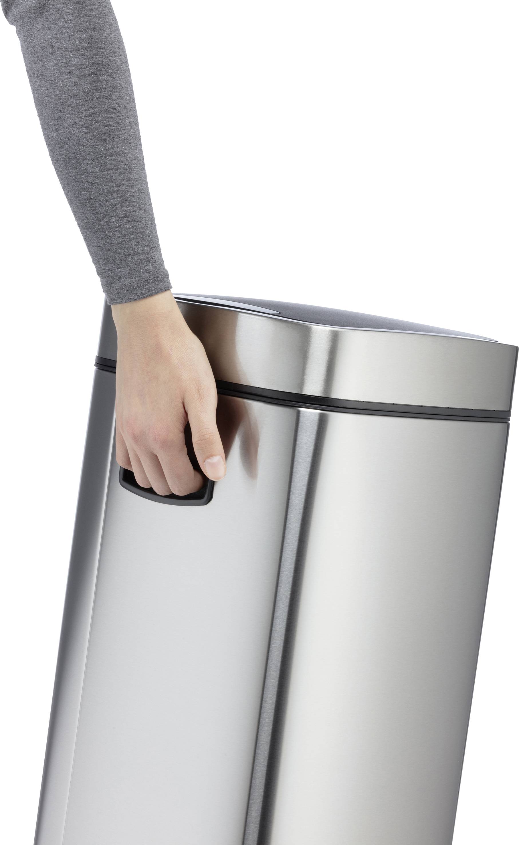 Eine Person öffnet den Deckel eines silbernen Mülleimers mit der Hand. Der Mülleimer hat eine zylindrische Form.