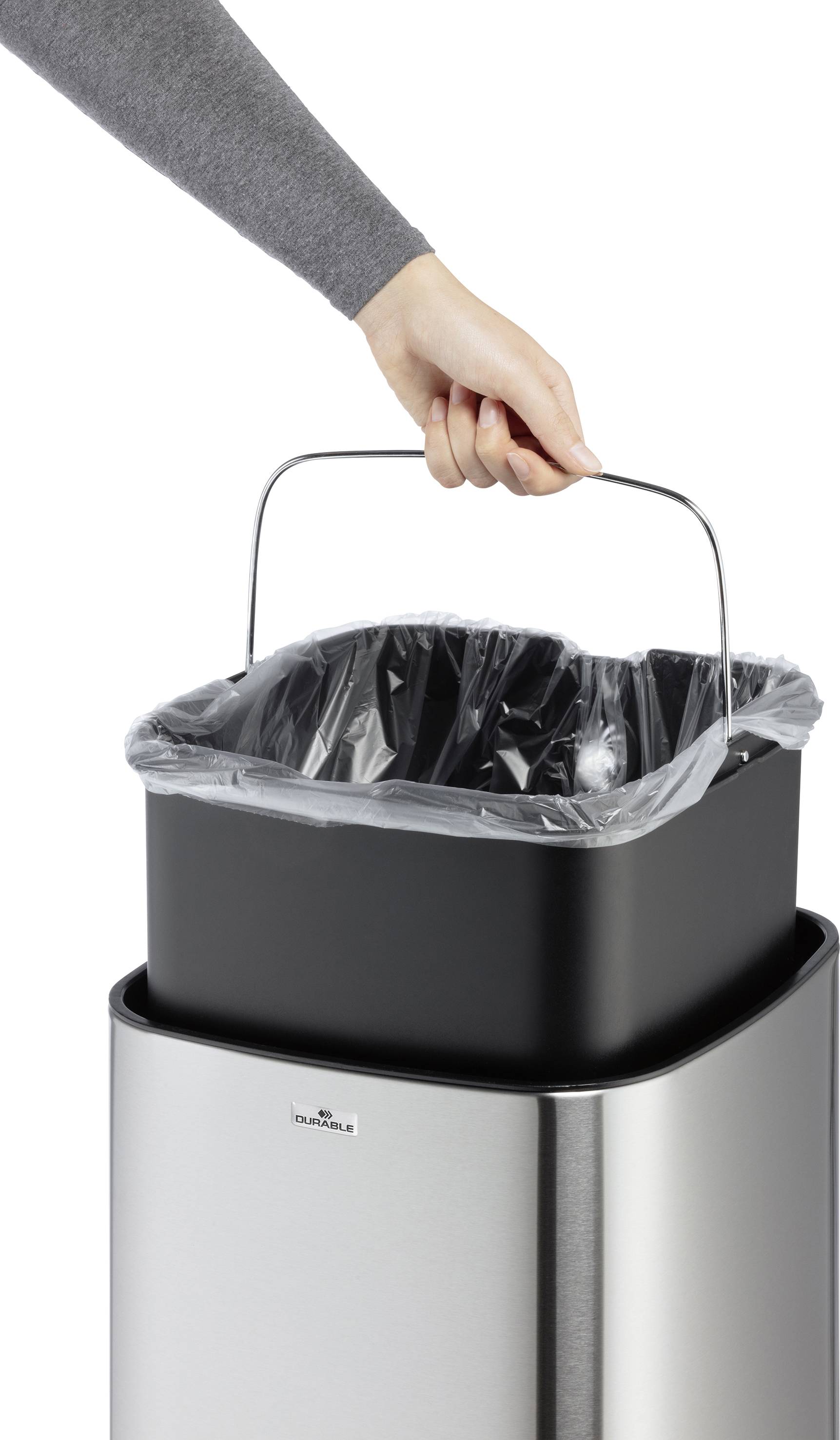 Eine Hand hebt einen schwarzen Mülleimer mit einem Metallgriff aus einem silbernen Abfallsammler.