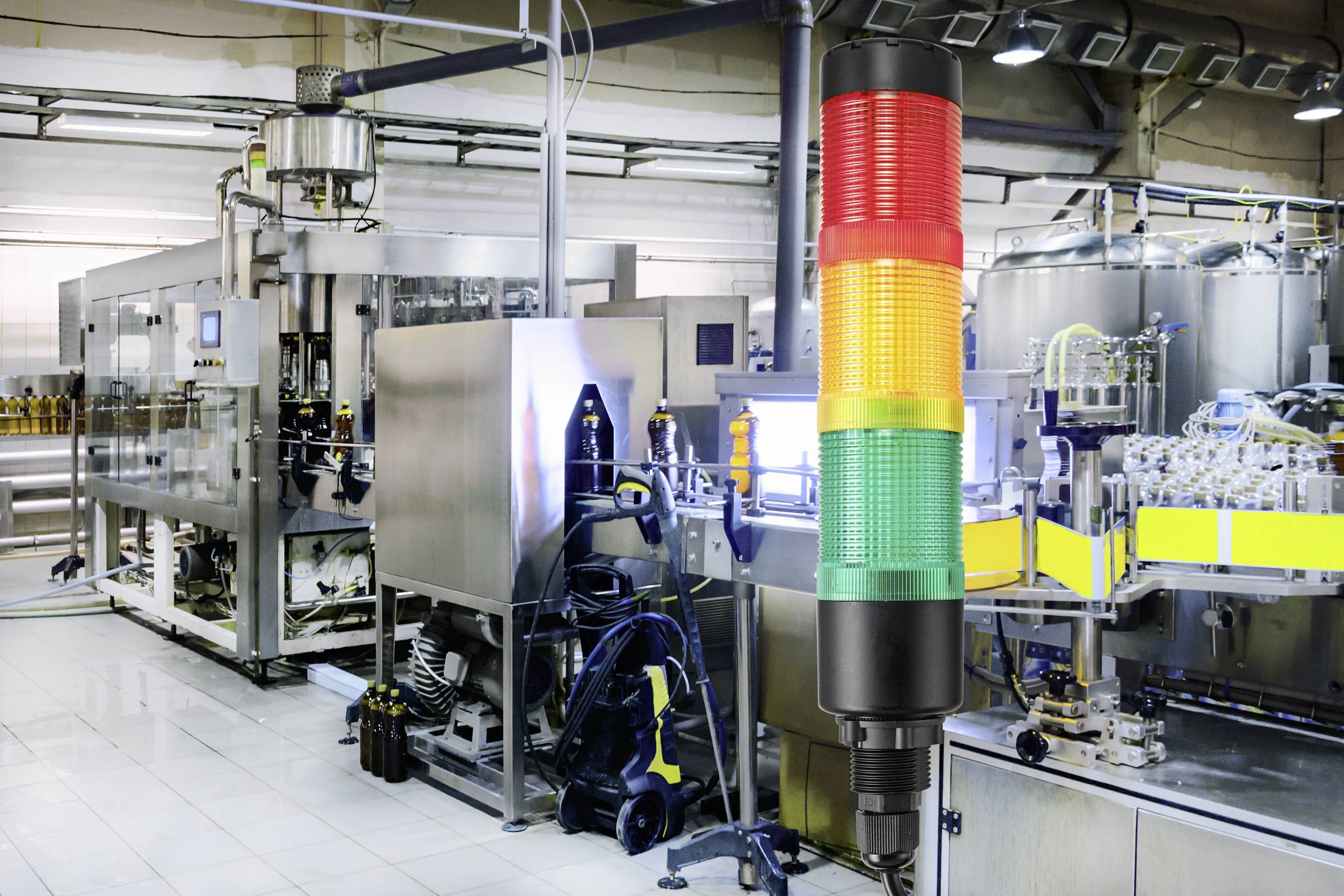 Fließband in einer Fabrik mit modernen Maschinen im Hintergrund; im Vordergrund eine mehrfarbige Signal-LED-Anzeige für Betriebsstatus.