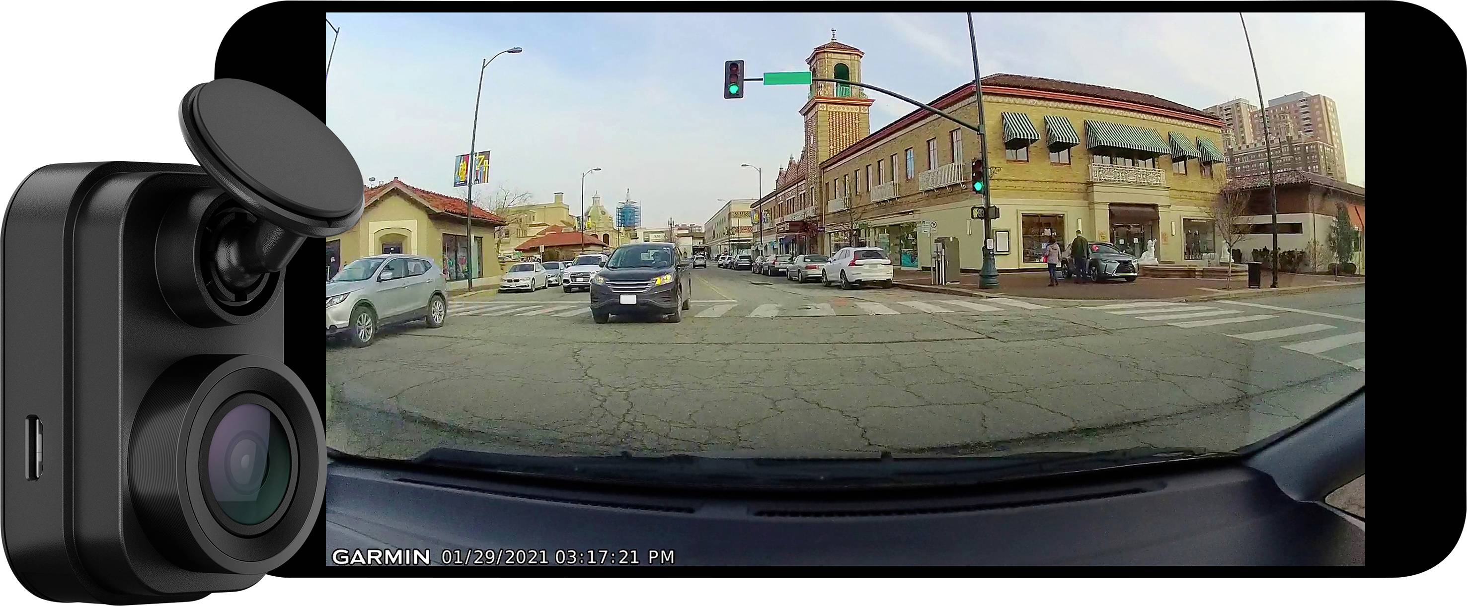 'Dashcam-Bild einer belebten städtischen Straßenkreuzung mit Autos und Geschäften bei Tageslicht, Ampel zeigt grün.'