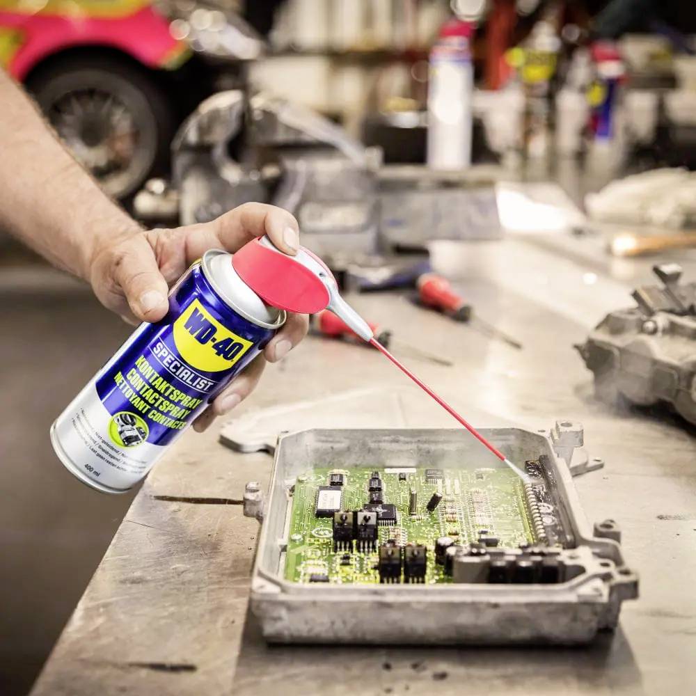 Ein Mensch sprüht WD-40 Specialist-Schmiermittel auf eine elektronische Leiterplatte, um Korrosion zu verhindern und Bauteile zu schützen.