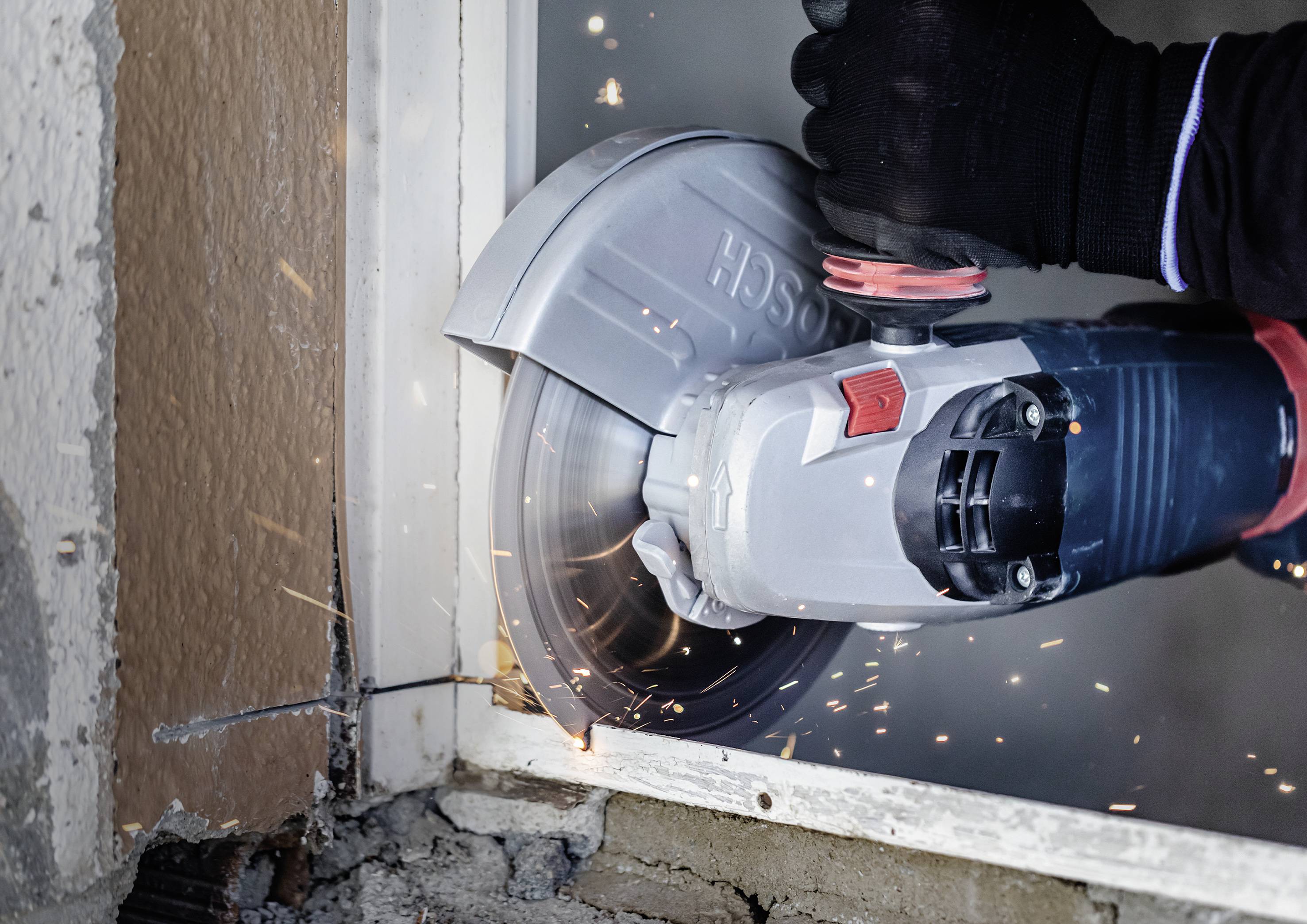 Eine Person schneidet mit einer elektrischen Schleifmaschine ein Metallstück in einem Rahmen. Funken fliegen beim Schneiden.