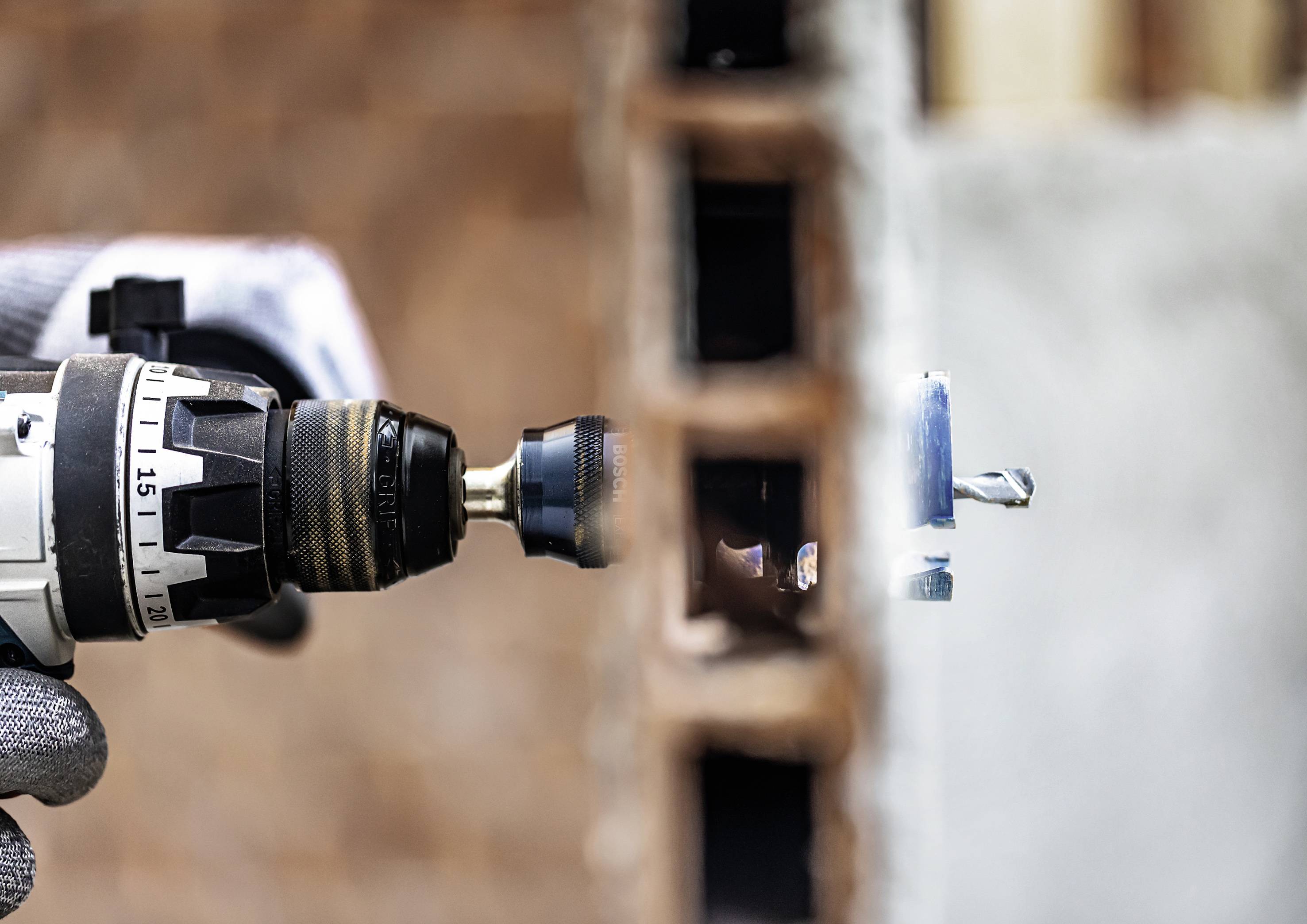 Ein Handwerker mit Handschuhen benutzt eine elektrische Bohrmaschine, um in eine Ziegelwand zu bohren. Staub und Trümmer fliegen.