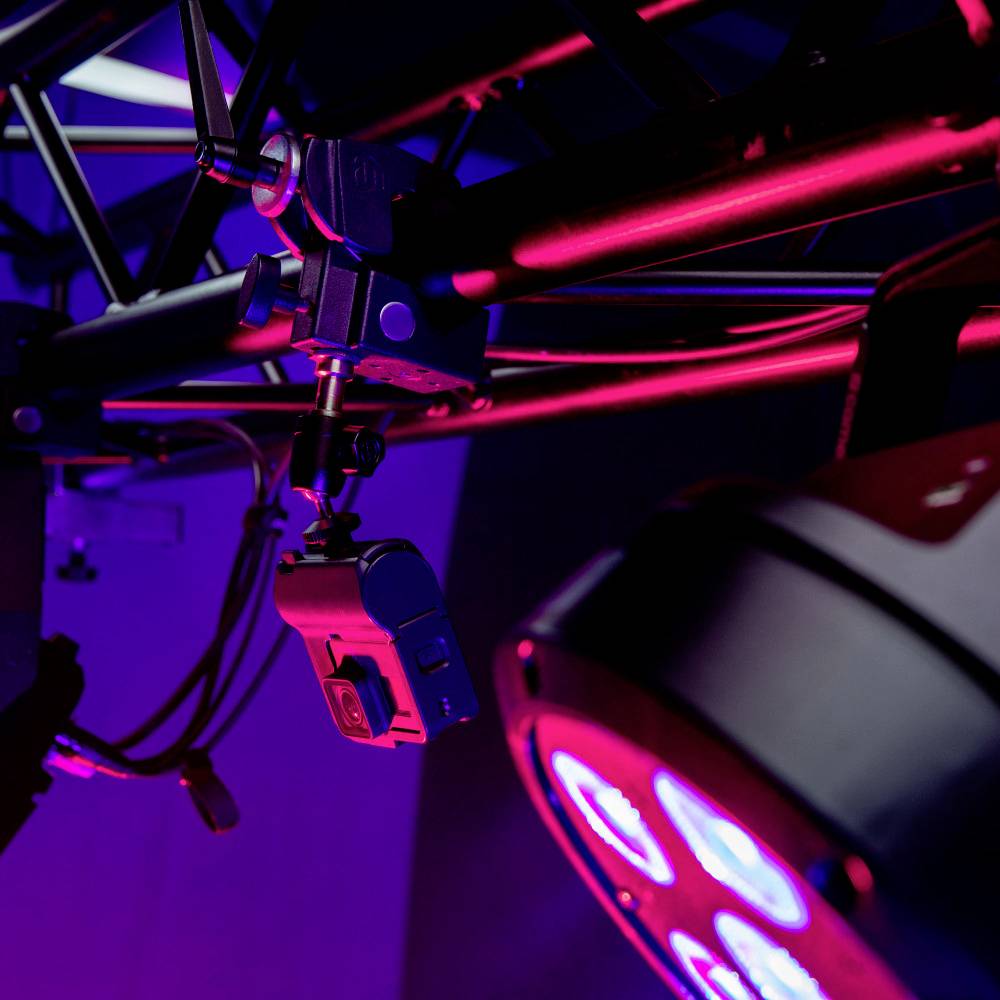 Industrielles Beleuchtungs- und Kamera-Setup mit blauen und rosa Lichtern an einer Stahlkonstruktion.