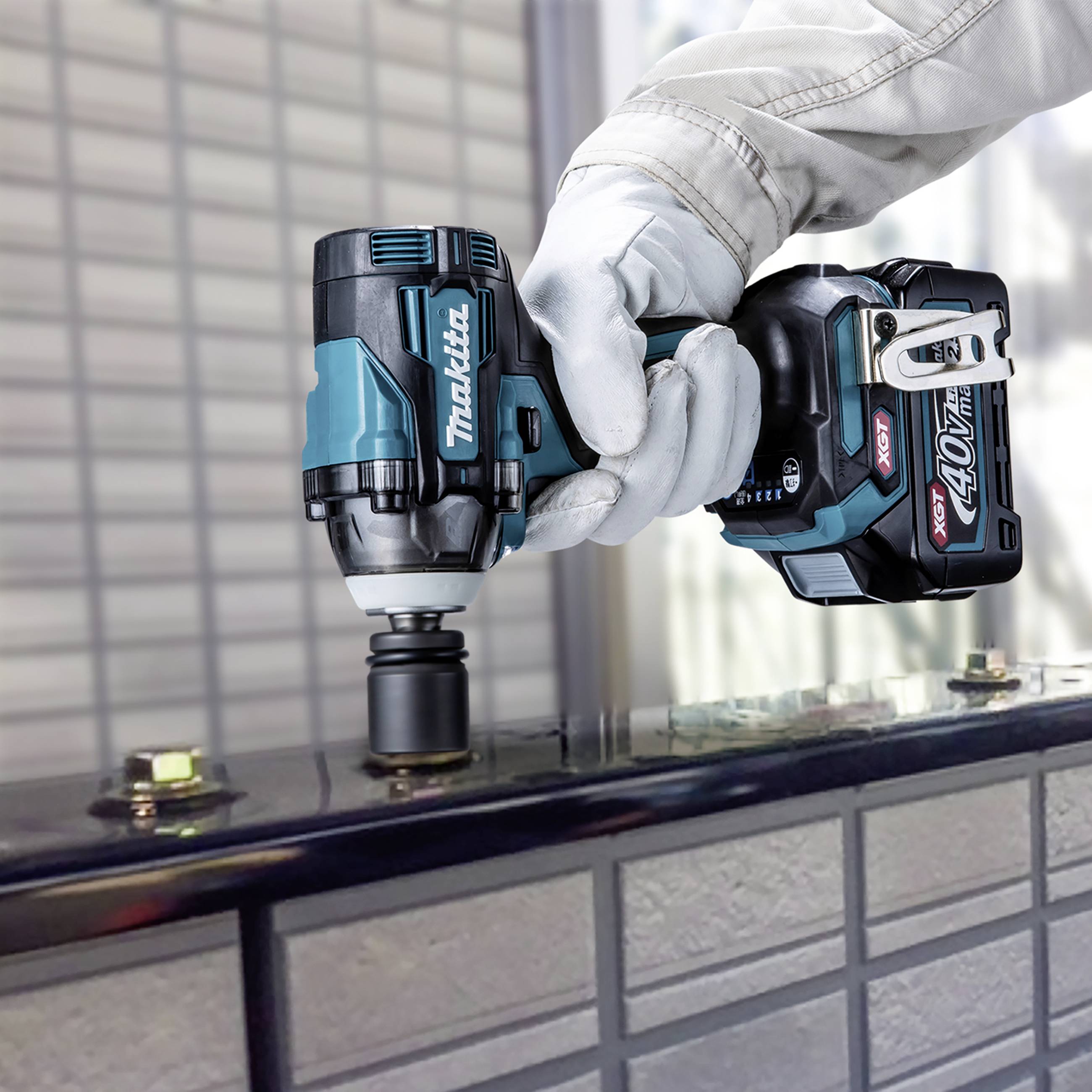Eine Person arbeitet mit einem akkugetriebenen Schraubenschlüssel von Makita an einem Metallobjekt. Im Hintergrund sind unscharfe Details.