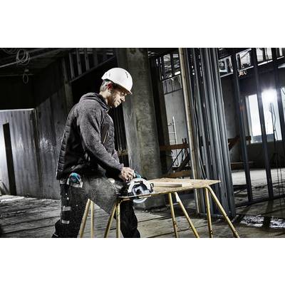 Ein Bauarbeiter mit Schutzhelm schneidet Holz mit einer Kreissäge in einem unfertigen Gebäude. Umgebend sind Metallrahmen sichtbar.