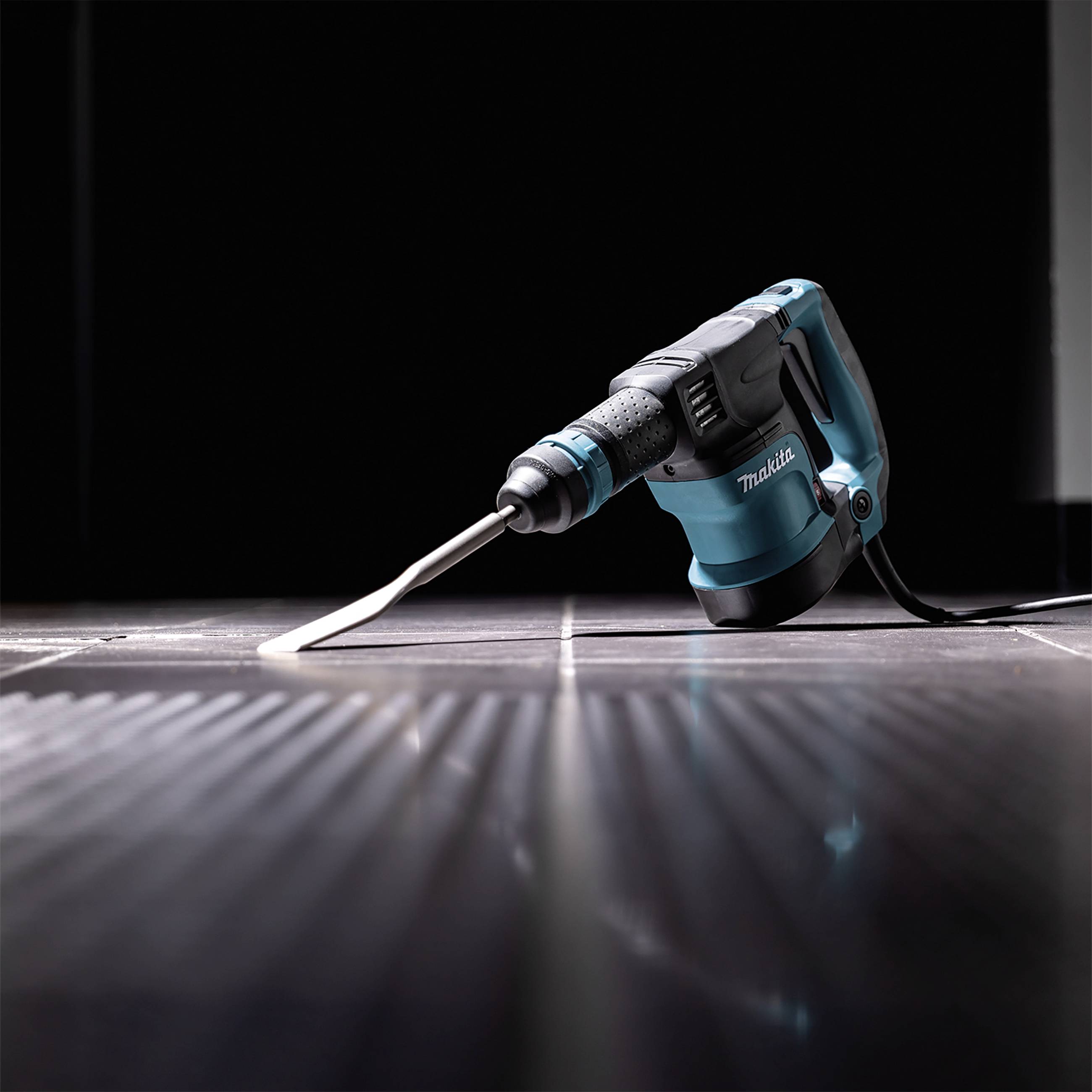 Ein elektrischer Bohrhammer liegt auf einem dunklen Boden und ist einsatzbereit. Das Gerät ist blau mit einem ergonomischen Griff.
