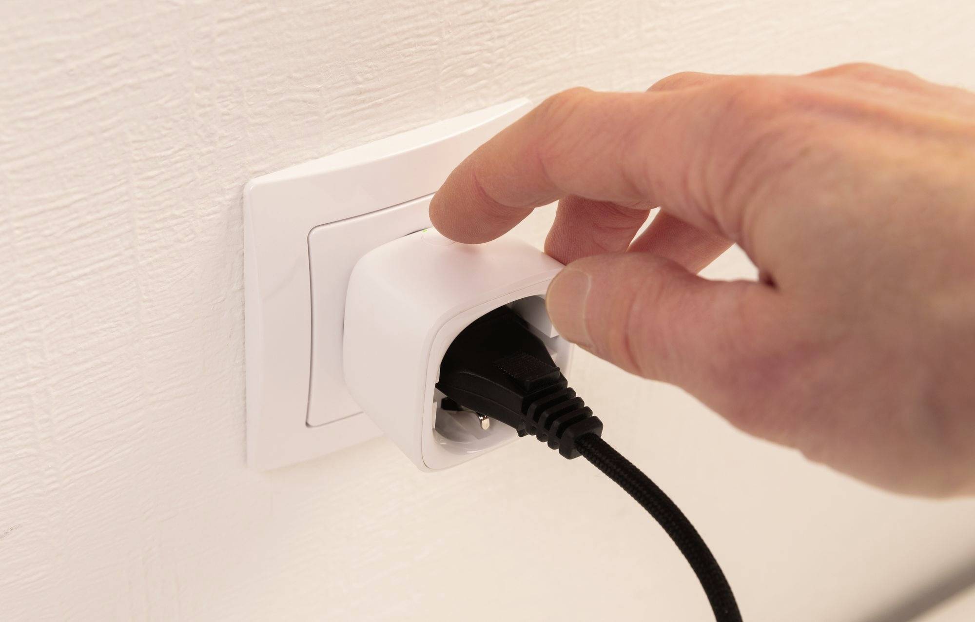 Eine Hand zieht einen schwarzen Stecker aus einer weißen Wandsteckdose heraus.