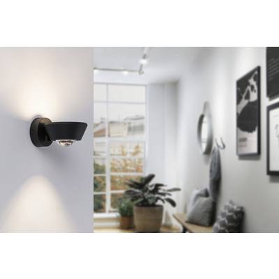 Eine moderne Wandleuchte beleuchtet einen hellen Flur mit Pflanzen und Bildern an der Wand. Ein großes Fenster im Hintergrund.