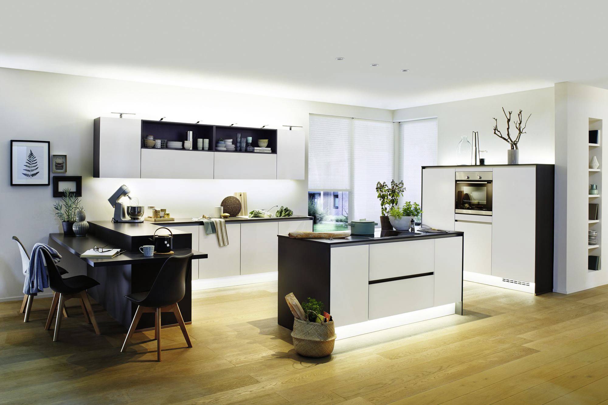 Moderne Küche mit hellen Schränken, einer Kücheninsel und Holzboden. Links: Esstisch mit Stühlen, rechts: eingebaute Geräte.