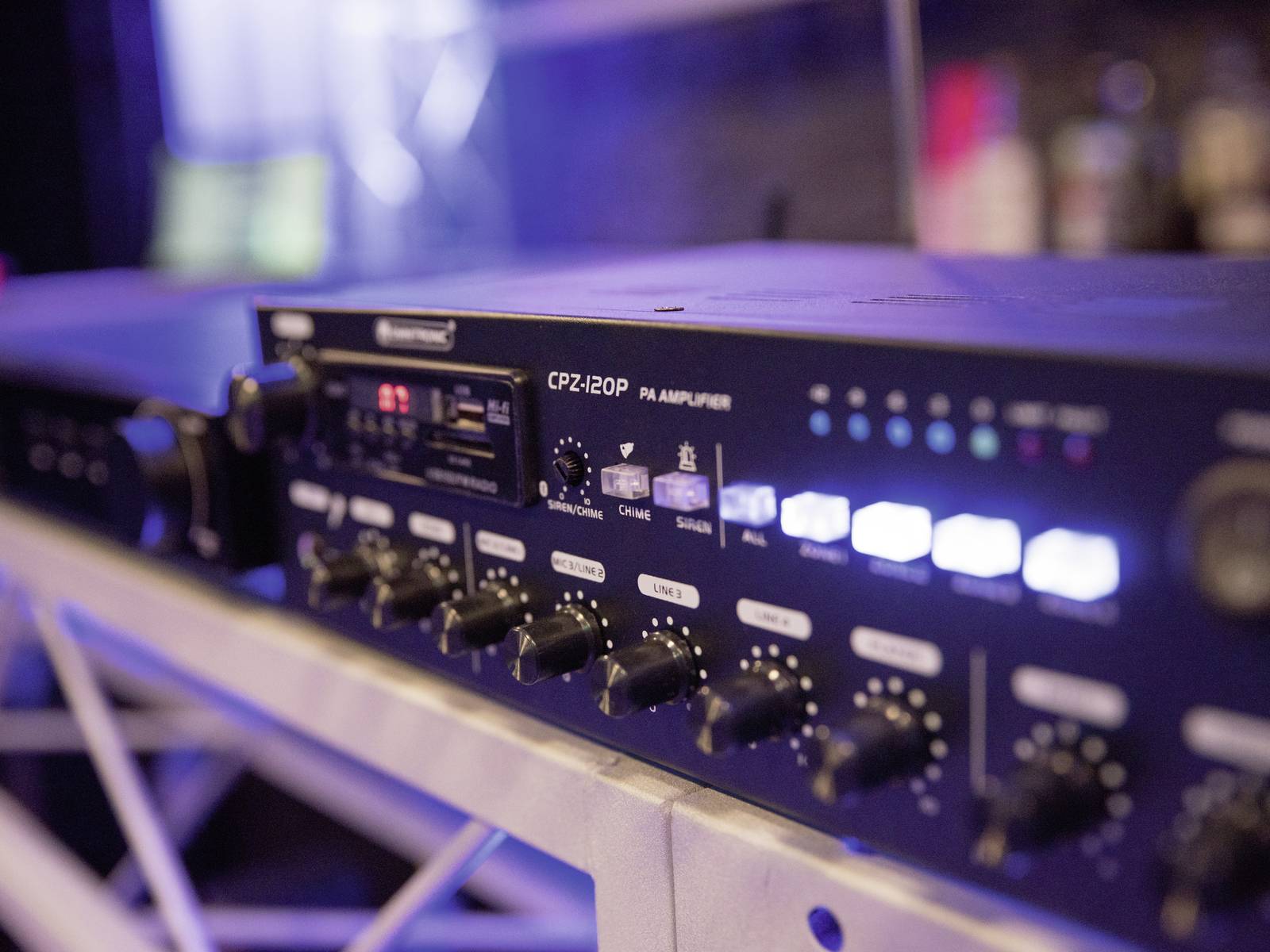 Ein PA-Verstärker auf einem Tisch mit mehreren Reglern und leuchtenden Anzeigen, vermutlich in einem Musikstudio oder Veranstaltungsraum.