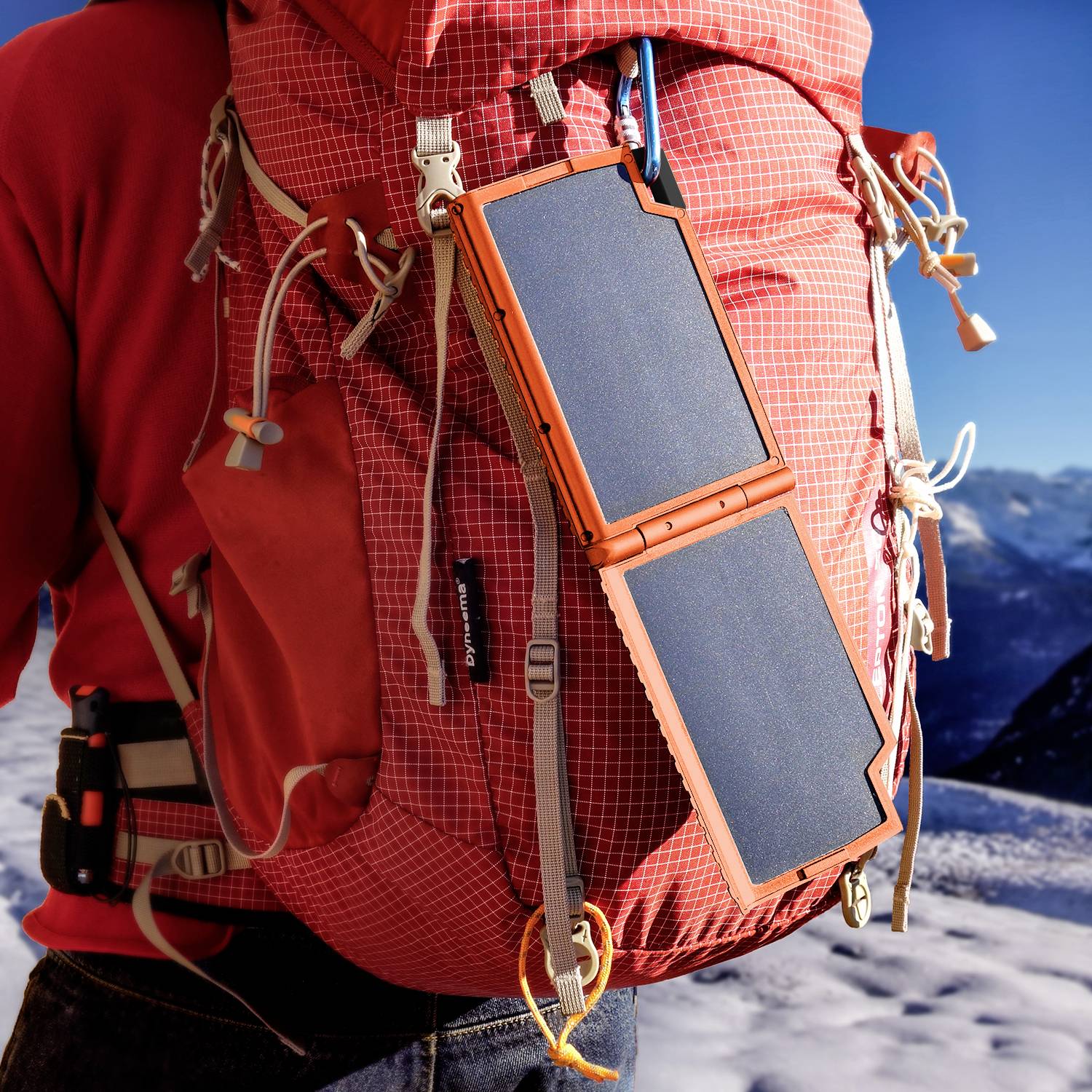 Ein person trägt einen roten Rucksack mit einem befestigten, faltbaren Solarladegerät; Hintergrund zeigt verschneite Berglandschaft.