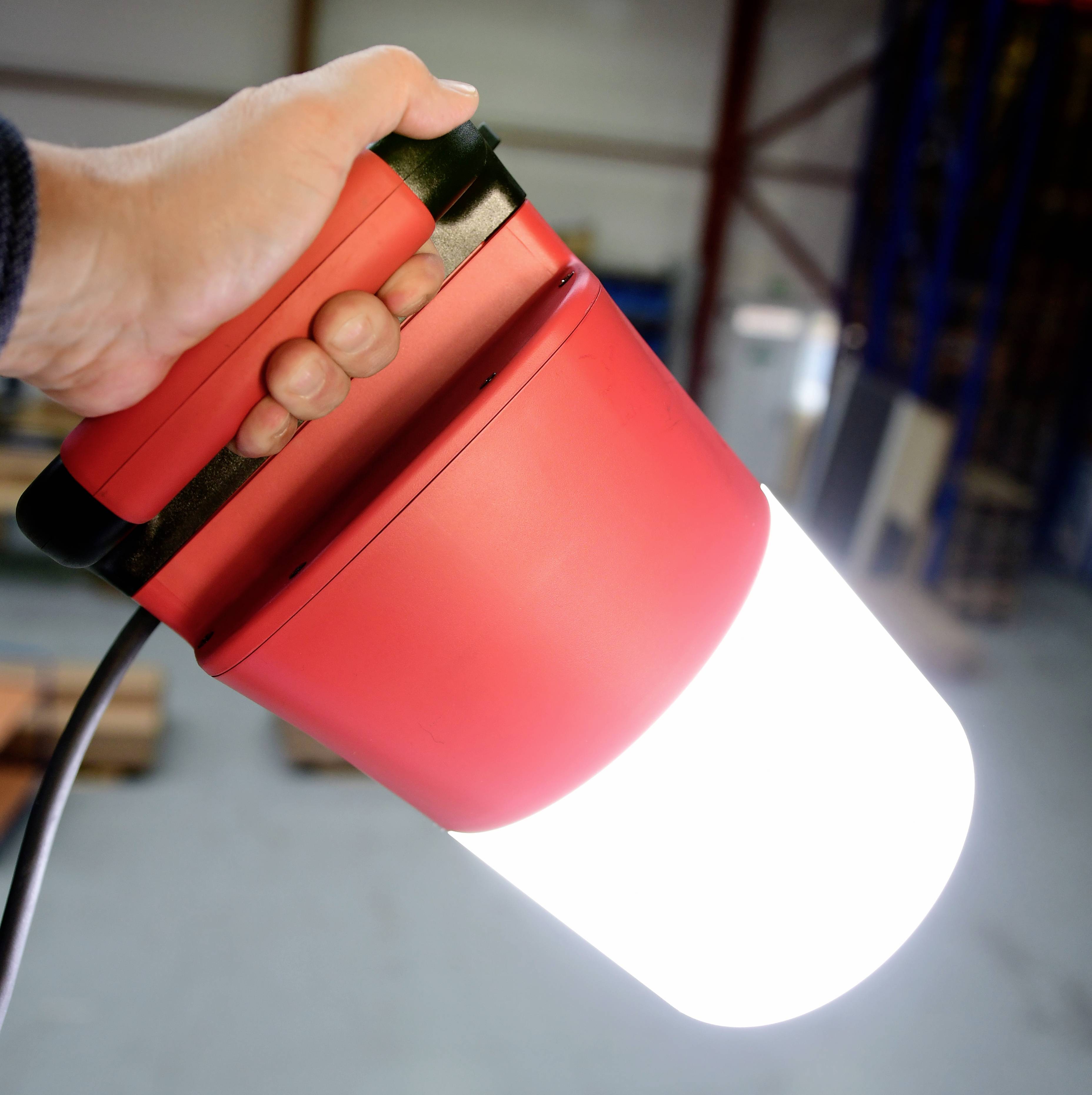 Ein Mensch hält eine leuchtende, rote Taschenlampe in der Hand. Die Umgebung ist ein Lagerhaus mit Regalen.