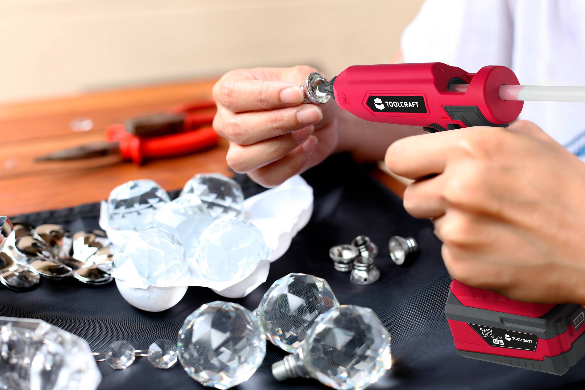 Eine Person benutzt eine Heißklebepistole, um Kristallkugeln und Löffel auf einem schwarzen Stoff zu befestigen. Im Hintergrund liegen Zangen.