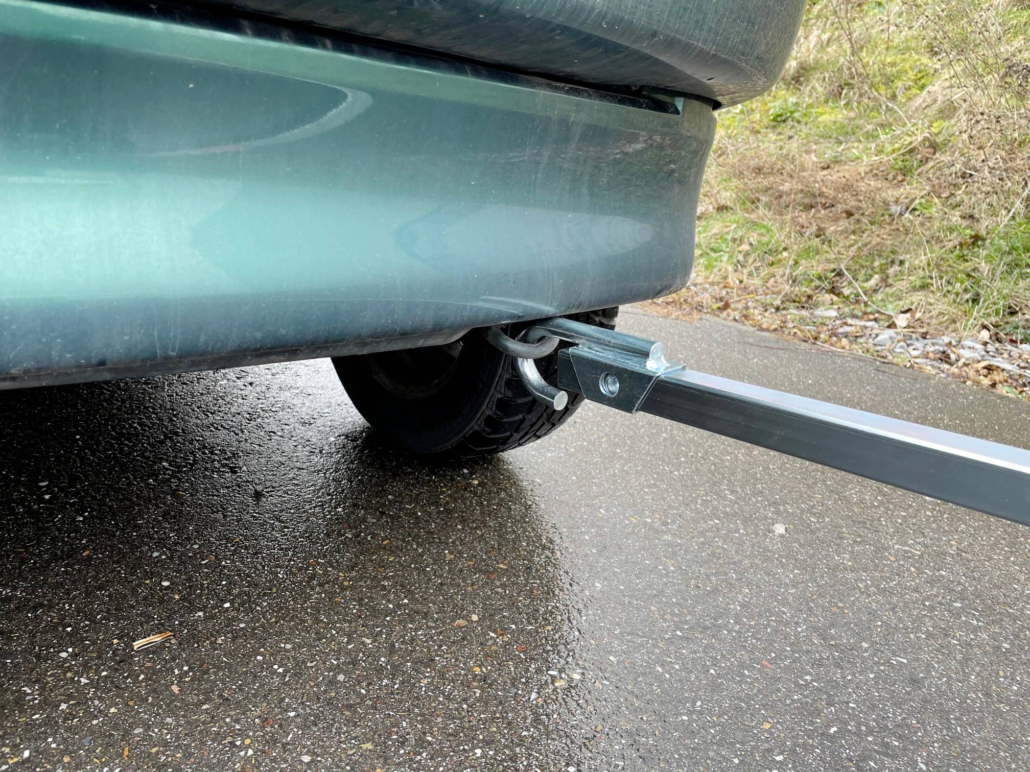 Ein Abschlepphaken ist an einem grünen Auto befestigt, das auf nasser Straße steht. Der Haken ist an einem Zugseil angebracht.