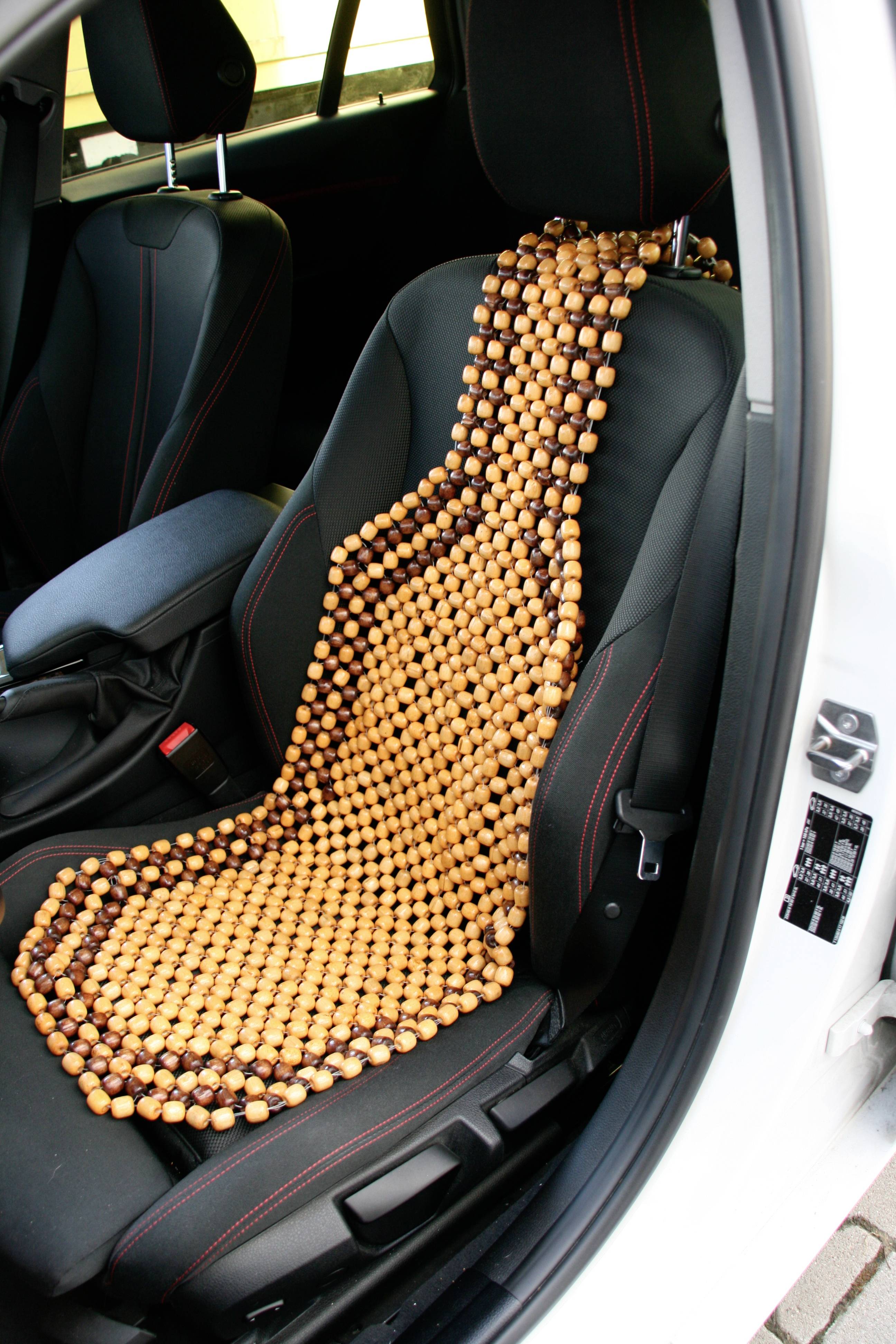 'Eine Autositzauflage aus Holzperlen liegt auf einem Fahrersitz in einem weißen Auto, um den Komfort der Sitzenden zu erhöhen.'