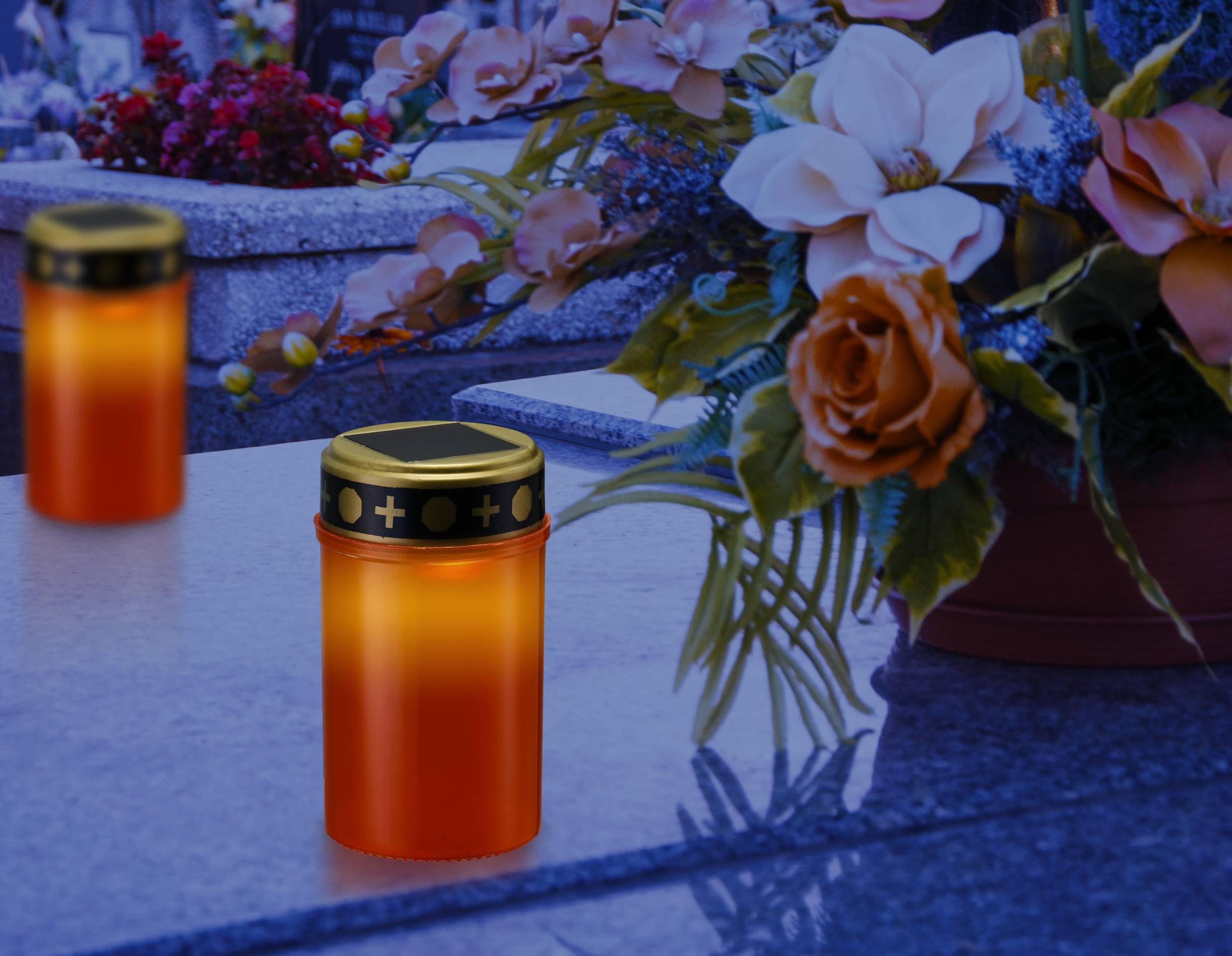 Kerzen auf einem Grabstein mit Blumenarrangement im Hintergrund, die eine Atmosphäre der Erinnerung und Ehrung schaffen.