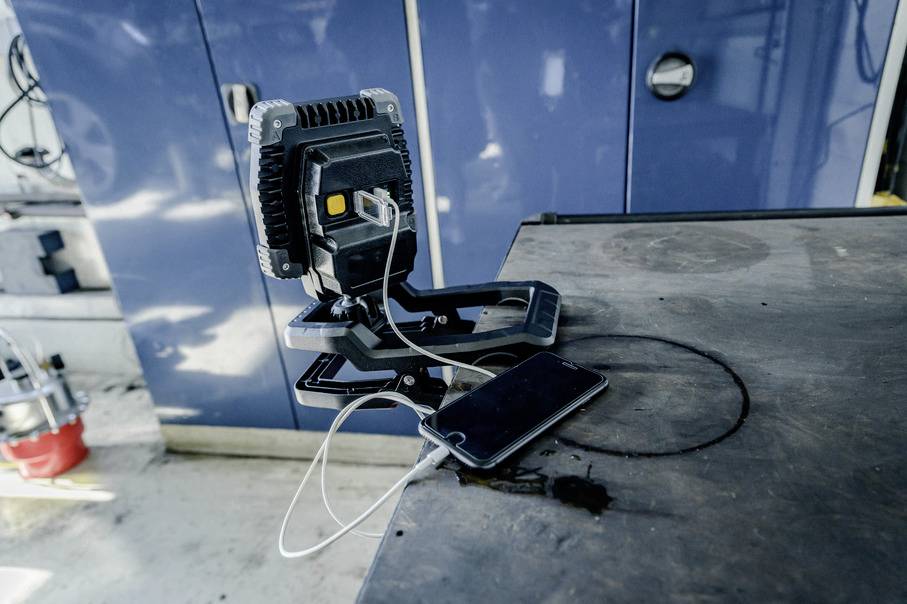 Ein Smartphone lädt auf einem Tisch über ein USB-Kabel, verbunden mit einem mobilen Ladegerät. Im Hintergrund sind blaue Schränke.