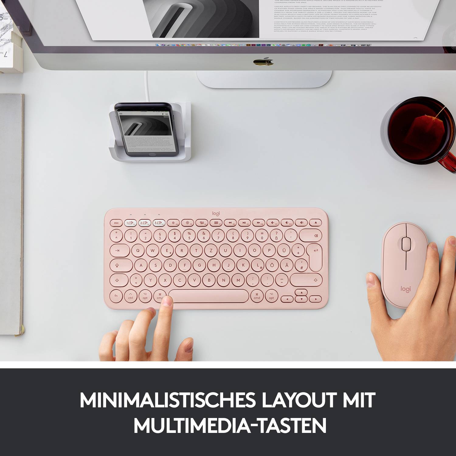 Eine rosa Tastatur und Maus auf einem Schreibtisch mit Computer und Kaffee, Text: 'Minimalistisches Layout mit Multimedia-Tasten'.