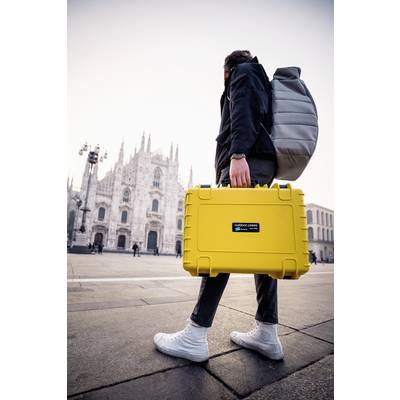 Eine Person in Freizeitkleidung trägt einen gelben Koffer und einen grauen Rucksack vor einer historischen Kathedrale auf einem Platz.