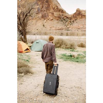 Eine Person zieht einen schwarzen Koffer auf einem Campingplatz in einer felsigen Landschaft mit Zelten im Hintergrund.