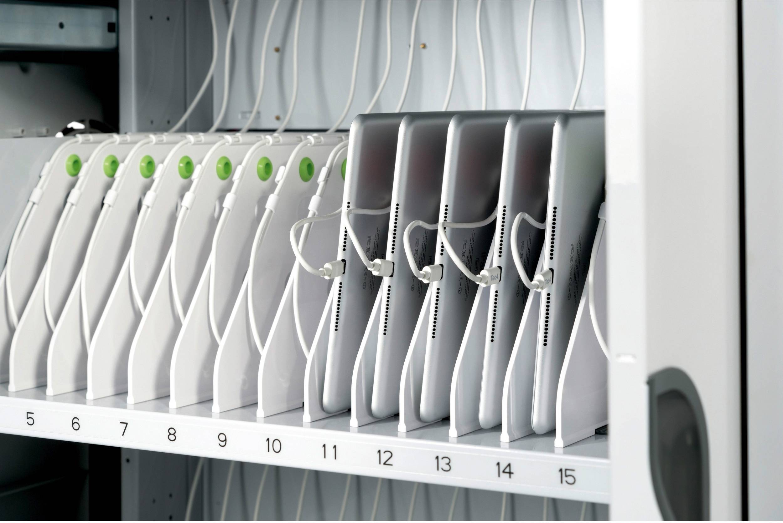 Tablett-Ladestation mit nummerierten Steckplätzen. Tablets sind zur Hälfte im Fach eingeschoben, verbunden mit Ladekabeln.